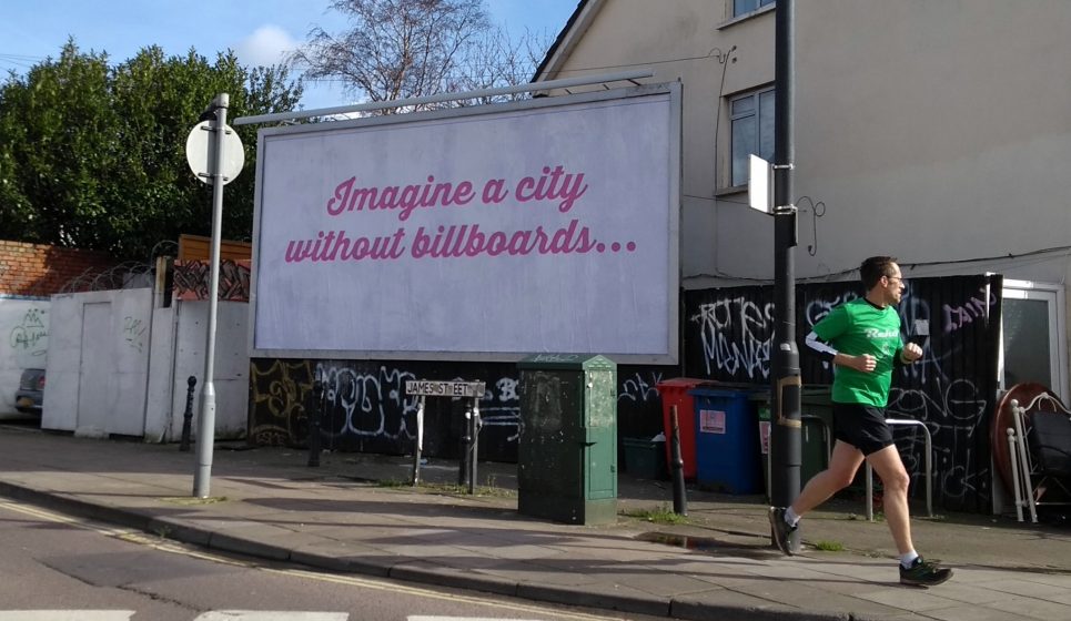A billboard in pink script reading "Imagine a city without billboards" with a person in activewear running by it