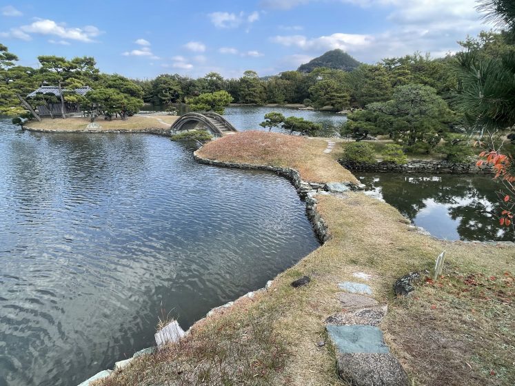 A body of water with trees and grass and a stone bridge over the water
