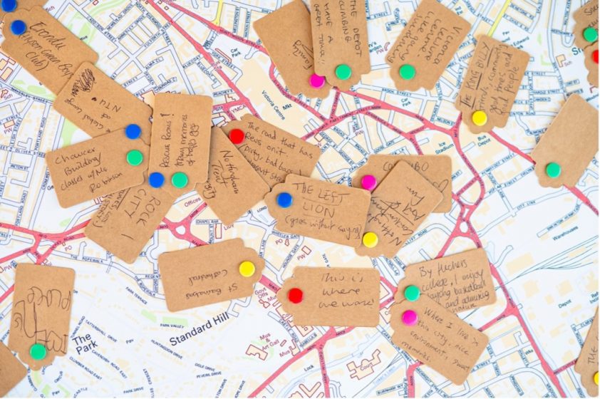 A group of brown tags with colorful pins on top of a map