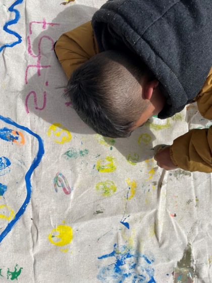 A child drawing on a large piece of canvas smattered with drawings and colorful squiggles