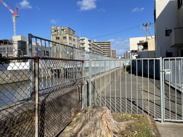 A metal gate blocking off a paved path next to a manmade waterway
