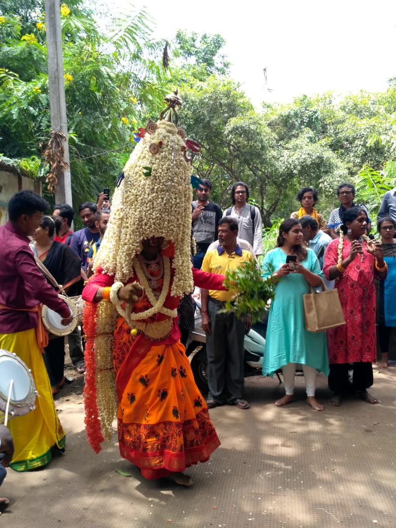 A person in an orange garment covered in white flower garlands with a large crowd of people around them