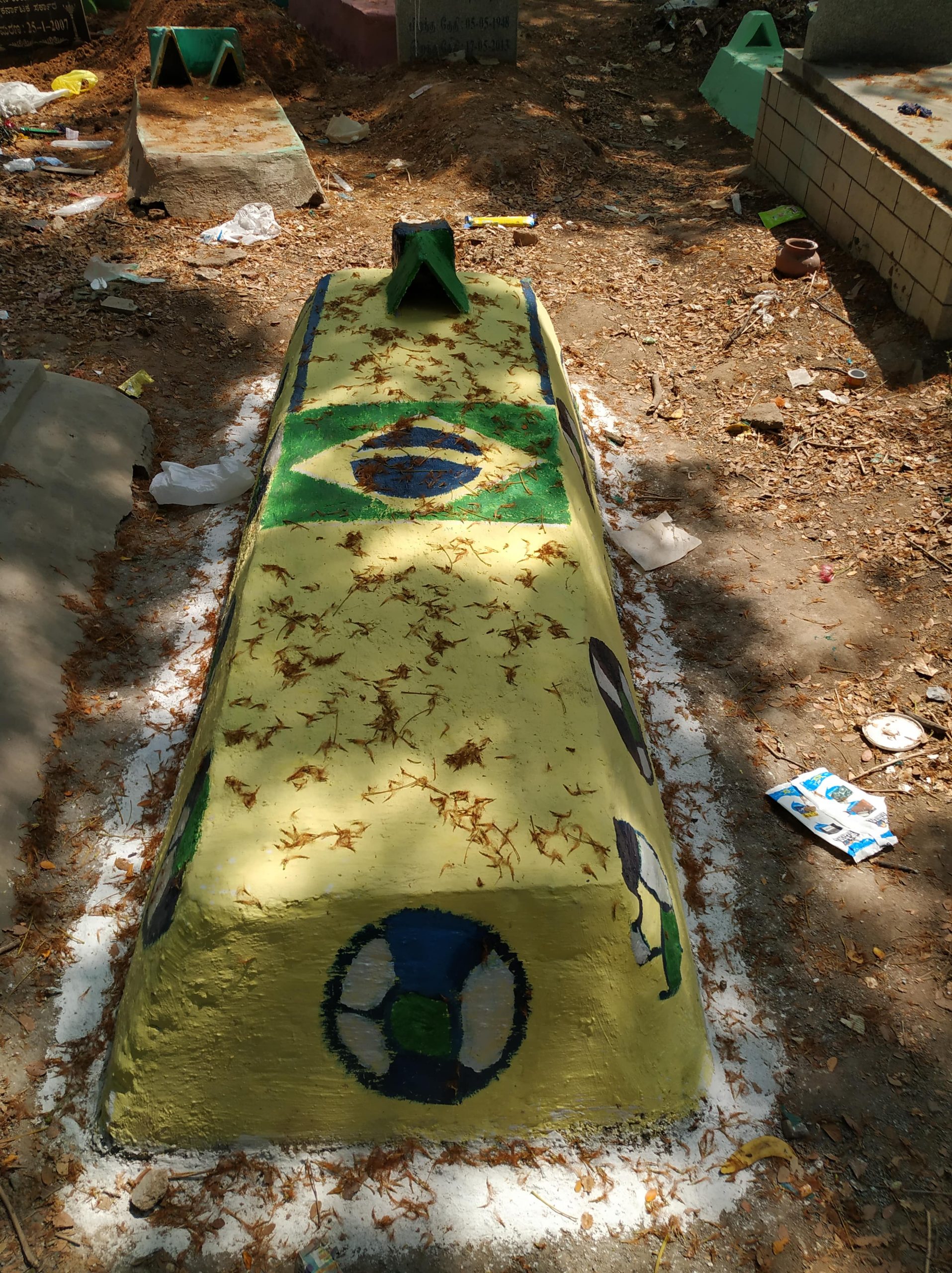 A coffin painted like the Brazilian flag in a mulched area 