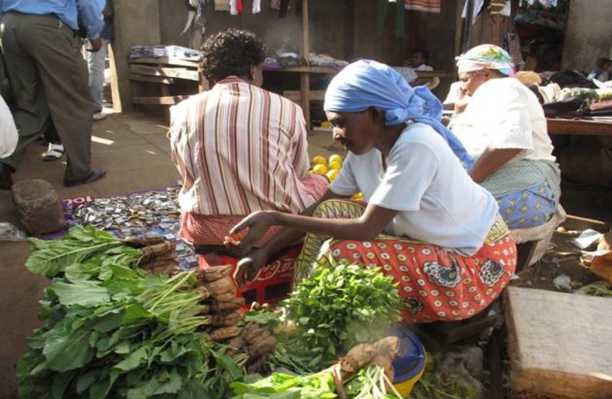 A person crouched down on the ground looking at green vegetables at a market