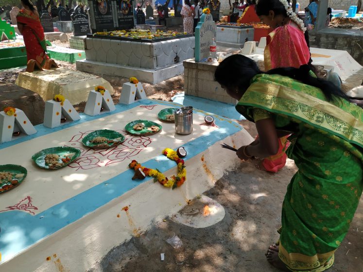 A blue and white grave with bowls of food placed atop it and people bowing around it