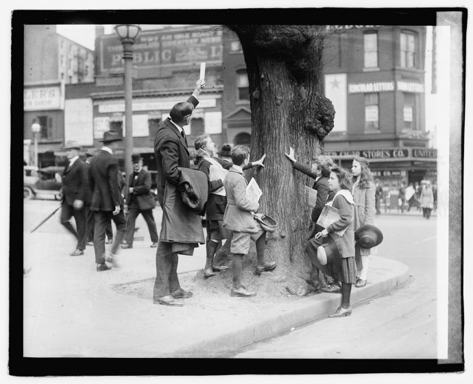 A black and white photo of a group of children reaching out to touch a tree