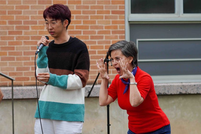 A group of play actors outside on stage talking into microphones and acting out a scene