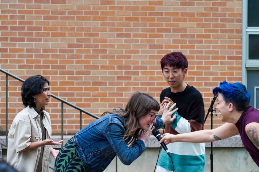 A group of play actors outside on stage talking into microphones and acting out a scene