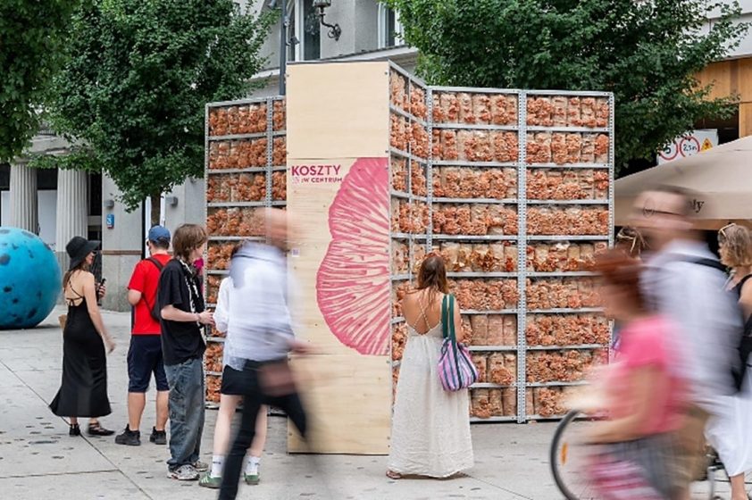 A picture of people walking past an art installation of shelves of bread on a sidewalk