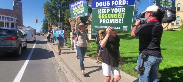 A picture of people holding signs, walking along a sidewalk