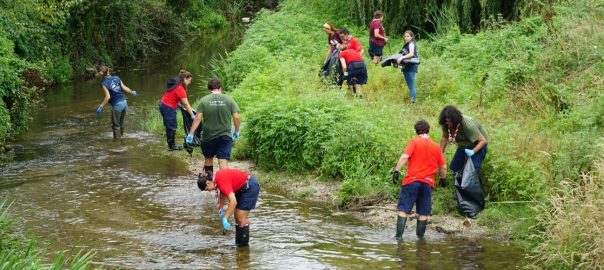 A group of people in a stream picking up trash