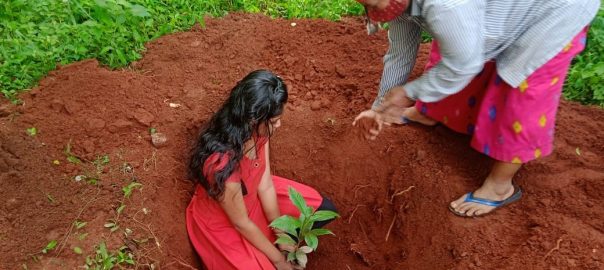 A young woman planting a plant in a deep hole with an older woman guiding her