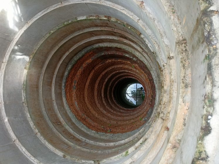 The inside of a deep concrete well showing water reflecting at the very bottom