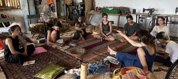 A group of people sitting in a circle on the floor talking to each other